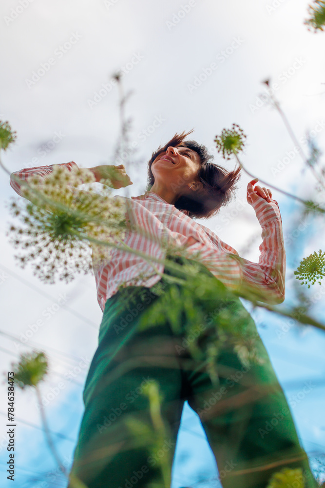 bright young girl in stylish clothes, wearing a pink shirt and green pants, poses against a background of blue sky and flowers. - obrazy, fototapety, plakaty 