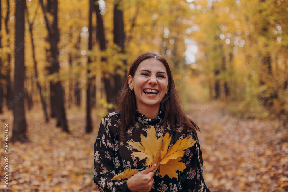 Portrait of young happy overjoyed woman with yellow leaf in hand having fun in autumn forest