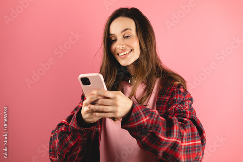Great application or website. Portrait of excited woman using her mobile phone, isolated on pink studio background, copy space. Positive lady holding gadget, looking at camera, texting, messaging.