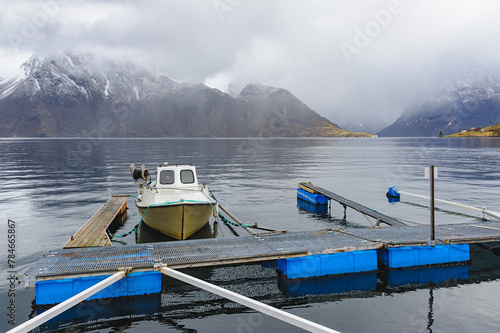 A solitary boat tied to a jetty, with tranquil waters and foggy mountains in the backdrop.