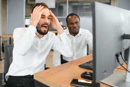 Two Unhappy tired businessman, corporate manager, sits at the workplace, tired from online work, stressed, nervous, massages the bridge of his nose, closed his eyes, experiencing a headache