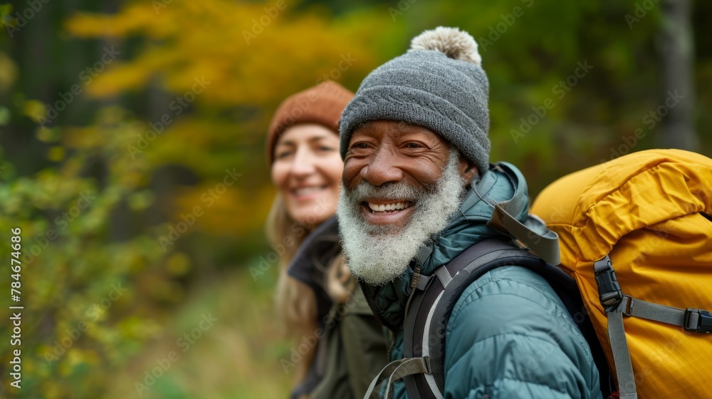 Joyful black elderly man and caucasian woman in warm hiking gear smiling in a colorful autumnal forest Joyful black elderly man and caucasian woman in warm hiking gear smiling in a colorful autumnal forest