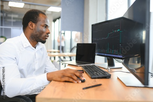 African-American broker works in office using workstation and analysis technology