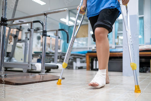 Medical care patient walking using crutches to support her injured ankle sprain, in the hospital physical therapist room. photo