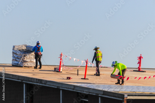 Принти на полотні A crew of construction workers atop a building prepare to install roofing underl