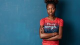 A confident young woman of African descent standing with her arms crossed in front of a deep blue wall t shirt with quote 