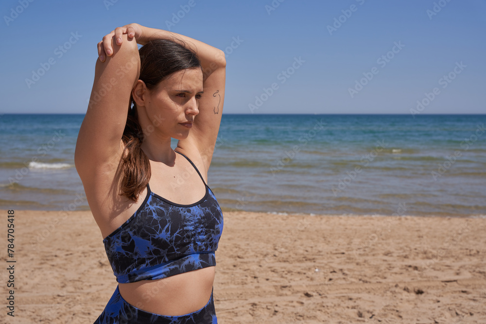 Healthy woman in sportswear stretching her arms on the beach