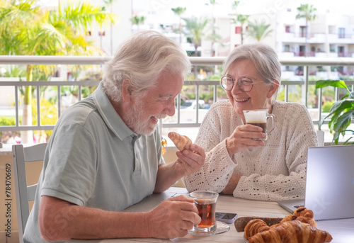Happy bonding senior retired couple have fun while enjoy breakfast together sitting outdoors on home terrace