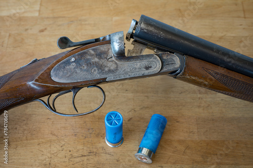 Detail of a nice old open parallel shotgun with some 12 gauge cartridges on a wooden table