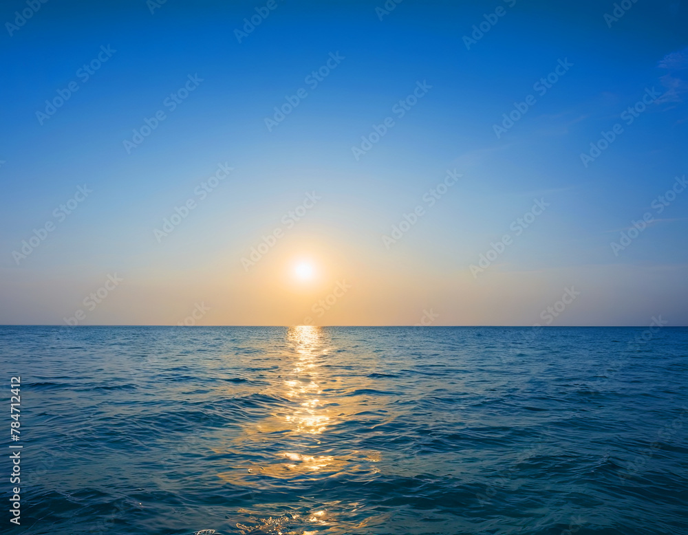 Obraz premium The sun is setting low over the ocean, casting a warm golden light across the water and creating a stunning reflection