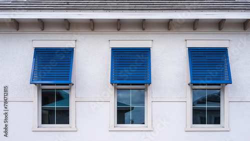 Closeup of three identical blue hurricane shutters on top halves of windows along exterior wall of an upscale single-family house under construction in a suburban development in southwest Florida
