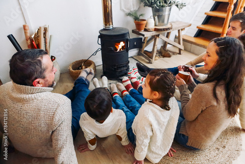 Cropped photo of big family wearing warm woolen socks resting by fireplace together in winter time. Mother, father and children lying on floor warming feet near potbelly stove in country house photo