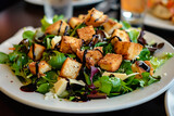 A plate of salad with a variety of greens and vegetables. The salad is garnished with croutons and a balsamic vinaigrette