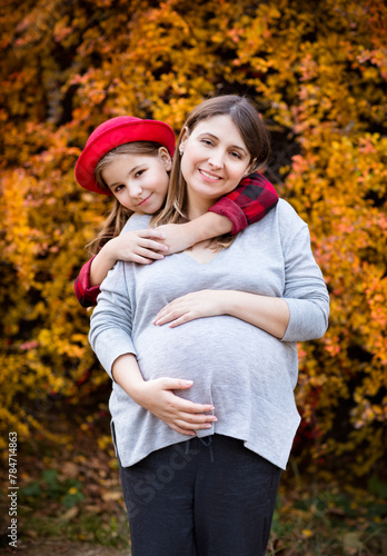 Happy young pregnant mother with daughter in autumn park
