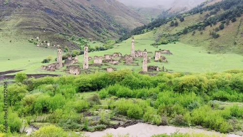 View of the medieval Targim tower complex in the Caucasus mountains surrounded by greenery. The Caucasus Mountains on a cloudy day in Ingushetia. Russia, 4K. photo