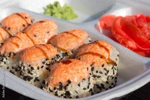 Baked sushi rolls with salmon, cheese and sauce on a foamed polystyrene tray.