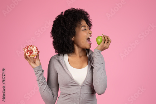 Lady choosing between donut and apple on pink background photo