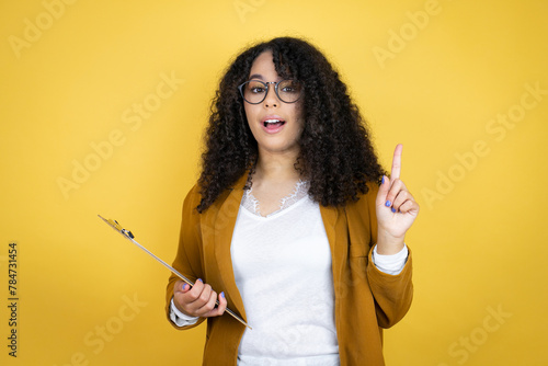 African american business woman with paperwork in hands over yellow background surprised and thinking with her finger on her head that she has an idea.