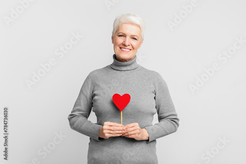 Elderly woman smiling with heart prop in hand