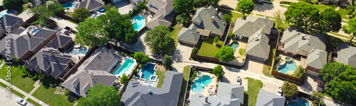 Panorama aerial view lush greenery suburban residential neighborhood subdivision, row upscale two-story houses, swimming pool, shingle roofing, large fenced backyard, well-trimmed HOA landscape