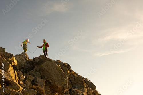 Two people are climbing a mountain. One of them is wearing a green shirt. The other person is wearing a red shirt