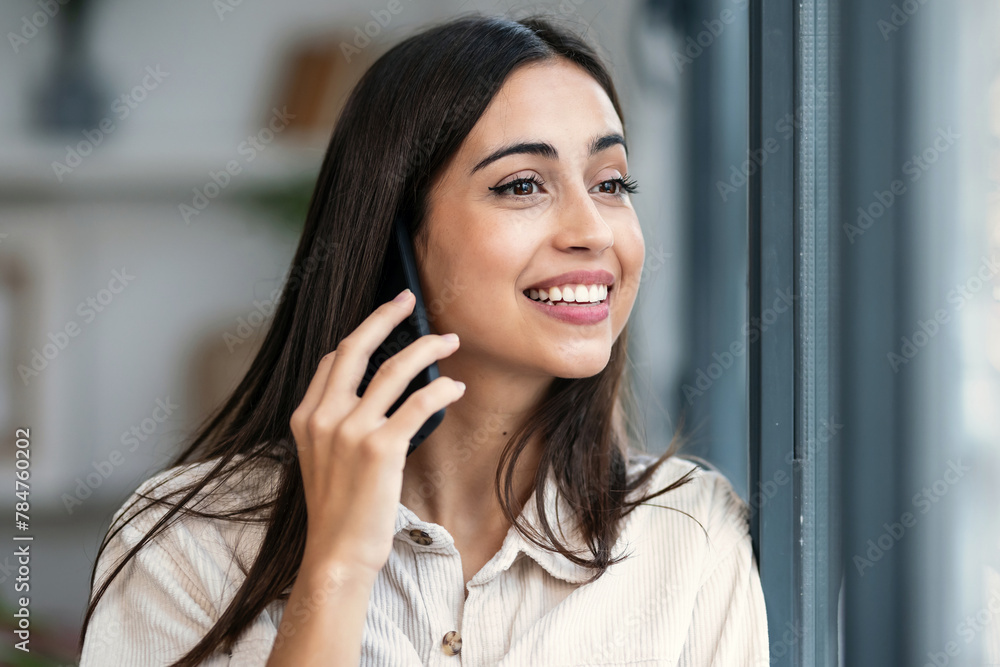 Beautiful woman talking with her mobile phone while standing next to the window at home Beautiful woman talking with her mobile phone while standing next to the window at home