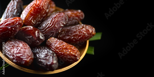 Dates fruit. Date fruits with palm tree leaf, in a wooden bowl, isolated on black background. Medjool dates close up. Border design © Subbotina Anna