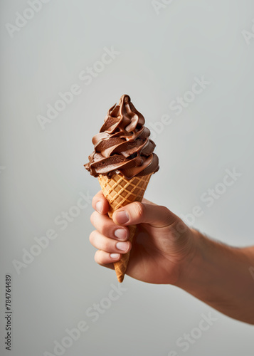 Hand holding chocolate ice cream with chocolate drops in wafer cup cone on grey background