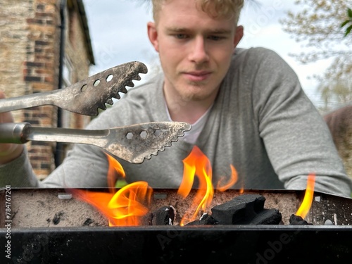 Selective focus on bbq grill fire, handsome man smiling on background holding grill tongs