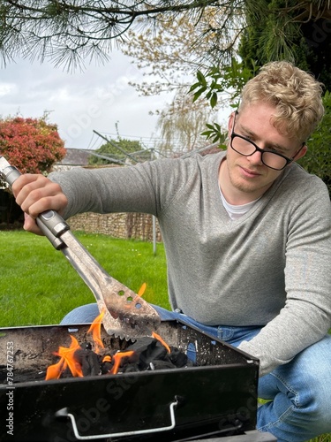 Vertical shot of a handsome man starting barbecue fire in the grill pit, using grill tongs