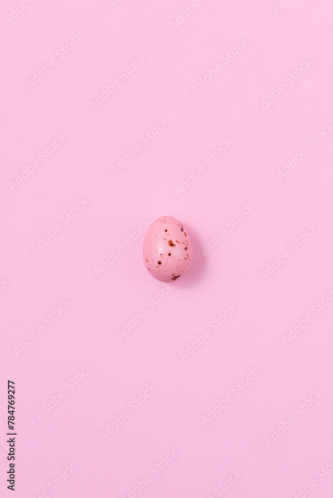 One speckled pink Easter egg casting a shadow on a pink background. Minimalism concept, copy space