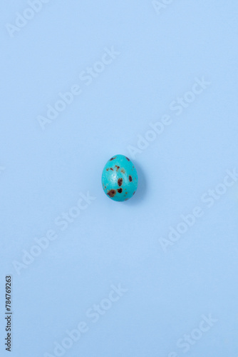 One speckled blue Easter egg casting a shadow on a blue background. Minimalism concept, copy space