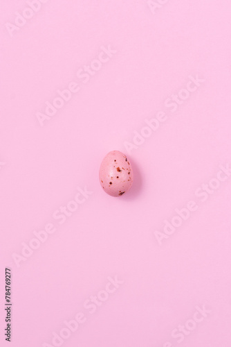 One speckled pink Easter egg casting a shadow on a pink background. Minimalism concept, copy space
