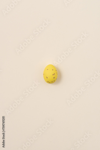 One speckled yellow Easter egg casting a shadow on a yellow background. Minimalism concept, copy space