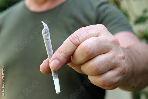 Ein Mann hält einen Joint zwischen den Fingern photo