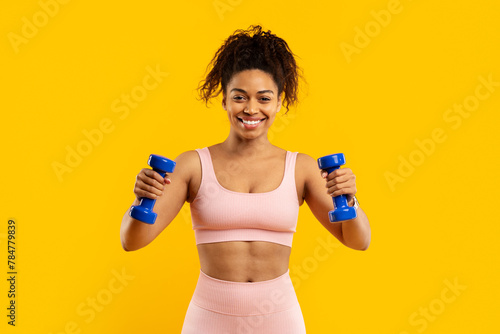 Smiling african american woman exercising with dumbbells © Prostock-studio