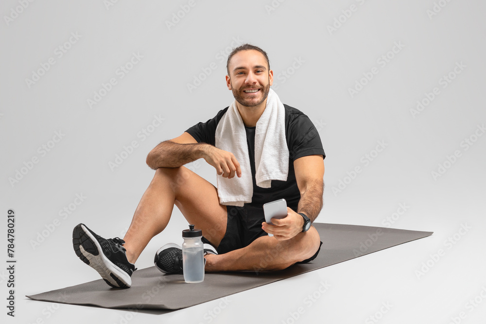 Fitness man with phone and water on mat Fitness man with phone and water on mat