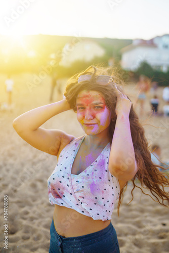 Happy woman covered in rainbow colored powder celebrating holi color festival. Young woman having fun with colorful powder outdoors. Beach party. Traditional Indian holiday. 