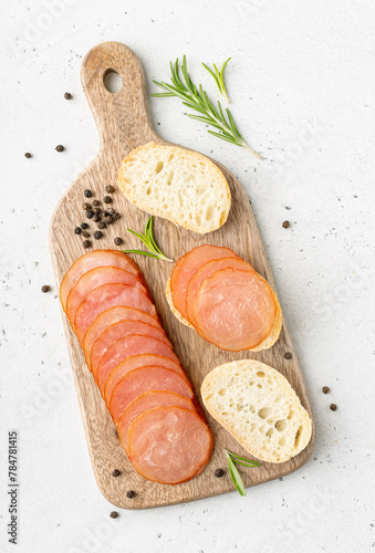 Slices of raw dried turkey served with fresh baguette on wooden board, top view