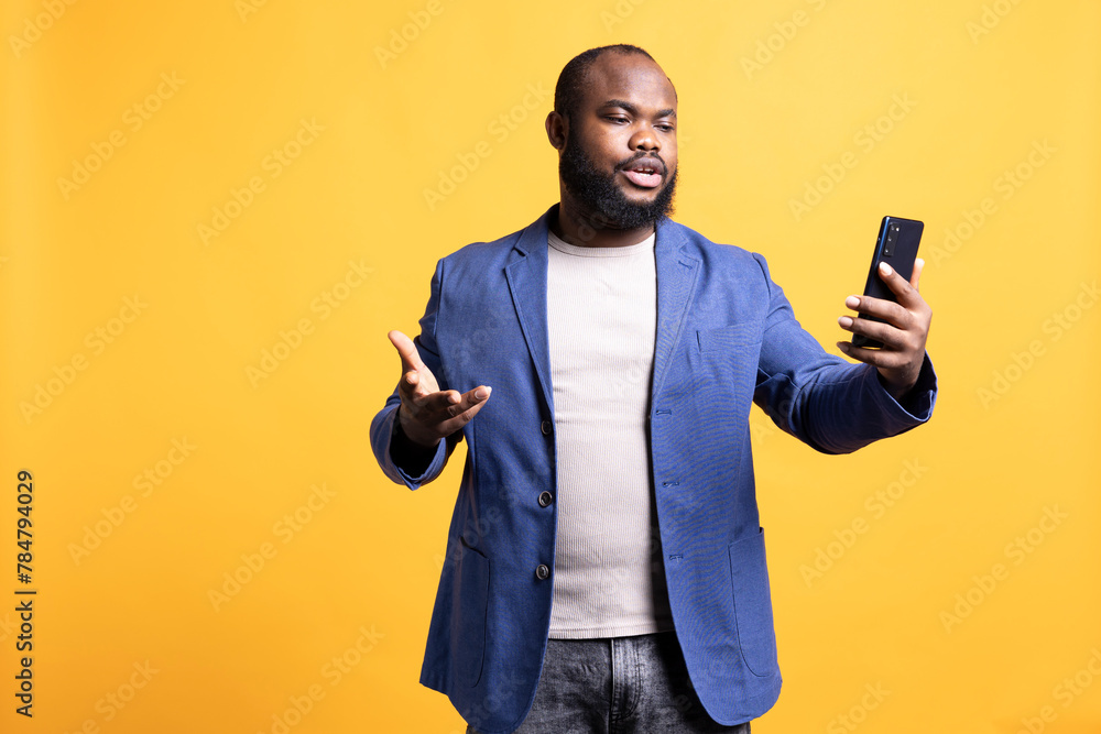 Annoyed man having unpleasant conversation with friends during teleconference meeting using smartphone, studio background. Hostile person having uncivil chat with mates during online videocall Annoyed man having unpleasant conversation with friends during teleconference meeting using smartphone, studio background. Hostile person having uncivil chat with mates during online videocall