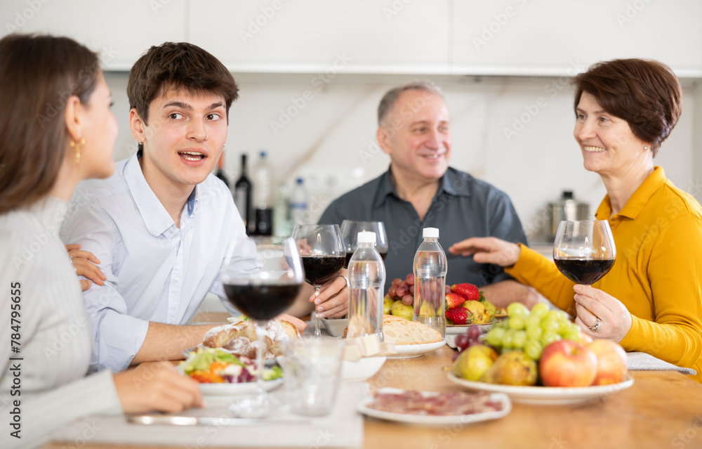 Smiling young man talking with family at festive table with wine and light snacks at home