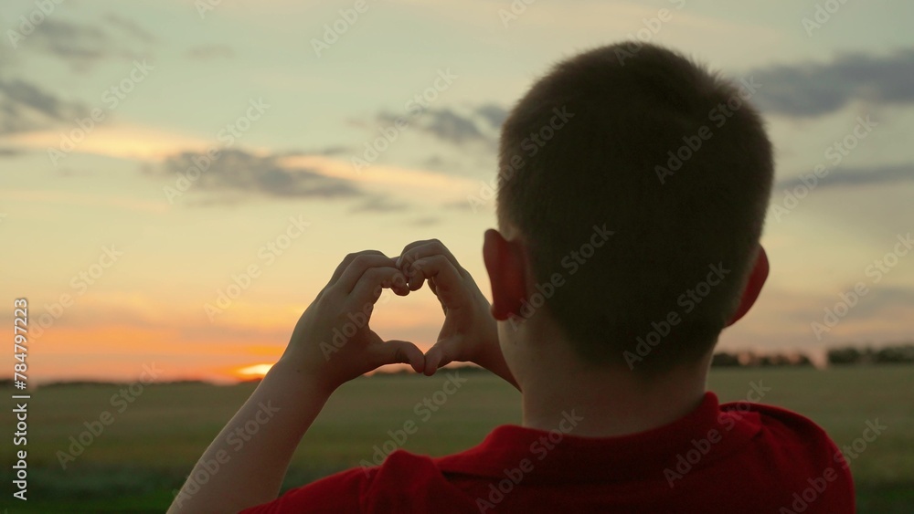 Children hands form heart symbol. Love, Health. Child boy plays sun in park, looks through symbol of heart at sky. Family love. Child makes heart shape with his fingers against sunset. Kid dream, Sky
