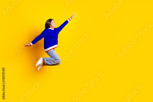 Full length photo of pretty teen girl jumping running fast superhero wear trendy knitwear blue outfit isolated on yellow color background