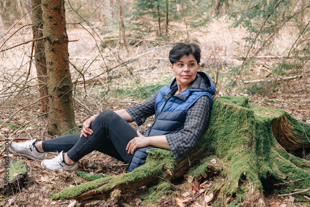 A woman in a coniferous forest rests leaning against a moss-covered stump A woman in a coniferous forest rests leaning against a moss-covered stump