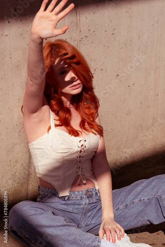 Beautiful red-haired girl with freckles in a fashionable outfit on a gray wall.
