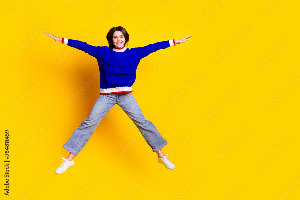 Full length photo of pretty teen girl jumping spread hands legs wear trendy knitwear blue outfit isolated on yellow color background