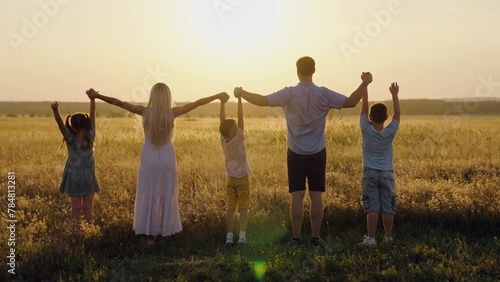 Parents kids holding hands together. Happy family raise their hands outdoor at sunset. Teamwork of group of people, walk in park. Child mom dad walking holding hands. Group prayer sun. Family holiday