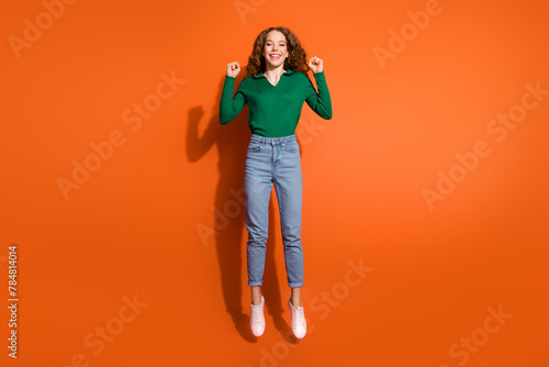 Full length photo of lucky excited lady dressed green shirt jumping high rising fists isolated orange color background