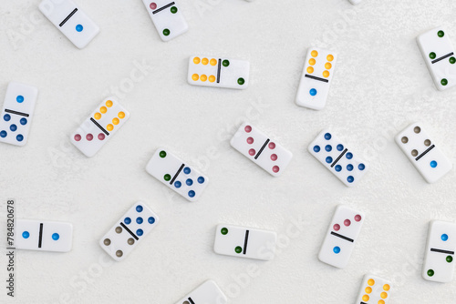 White dominoes with colorful dots on a white cement background, top view. Board game.