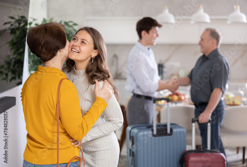Hospitable friendly young woman warmly greeting and kissing mother-in-law coming for cozy family dinner with set table in background..